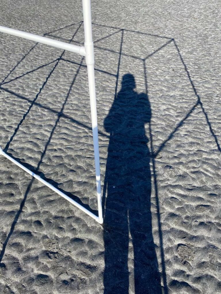 shadow of portable bus stop on the grey sand with person standing in it