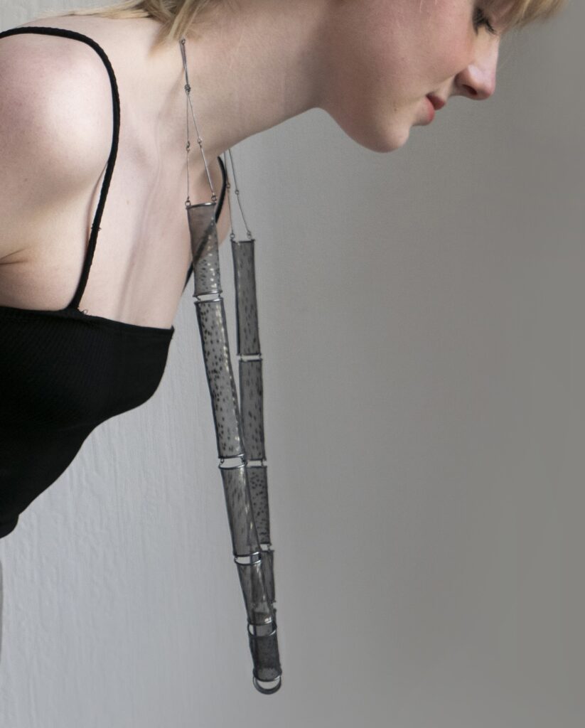 person wearing necklace, leaning so that it hangs away from the body.